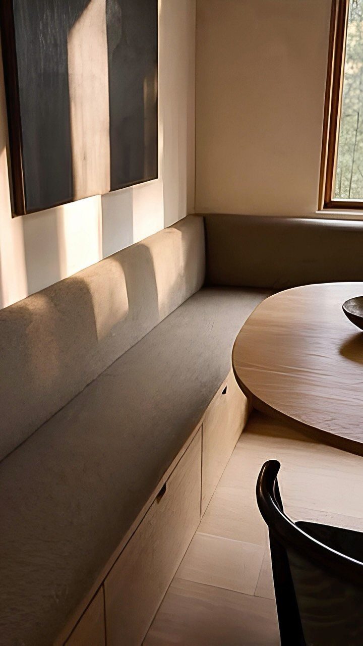 L-shaped built-in dining nook with grey upholstery and a round wooden table.