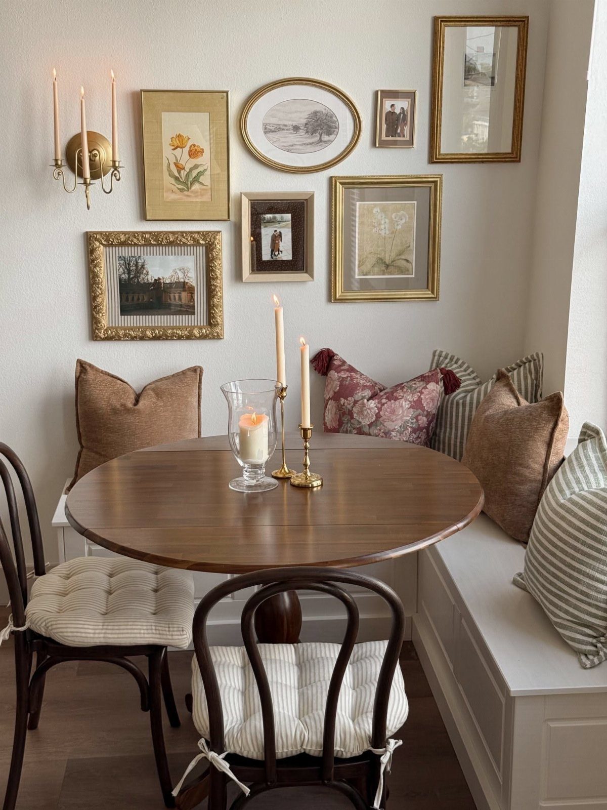Gallery wall of framed art above a round wooden dining table and built-in bench.