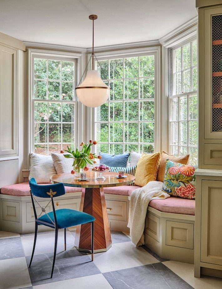 Round wooden pedestal table in a bright dining nook with built-in banquette seating.