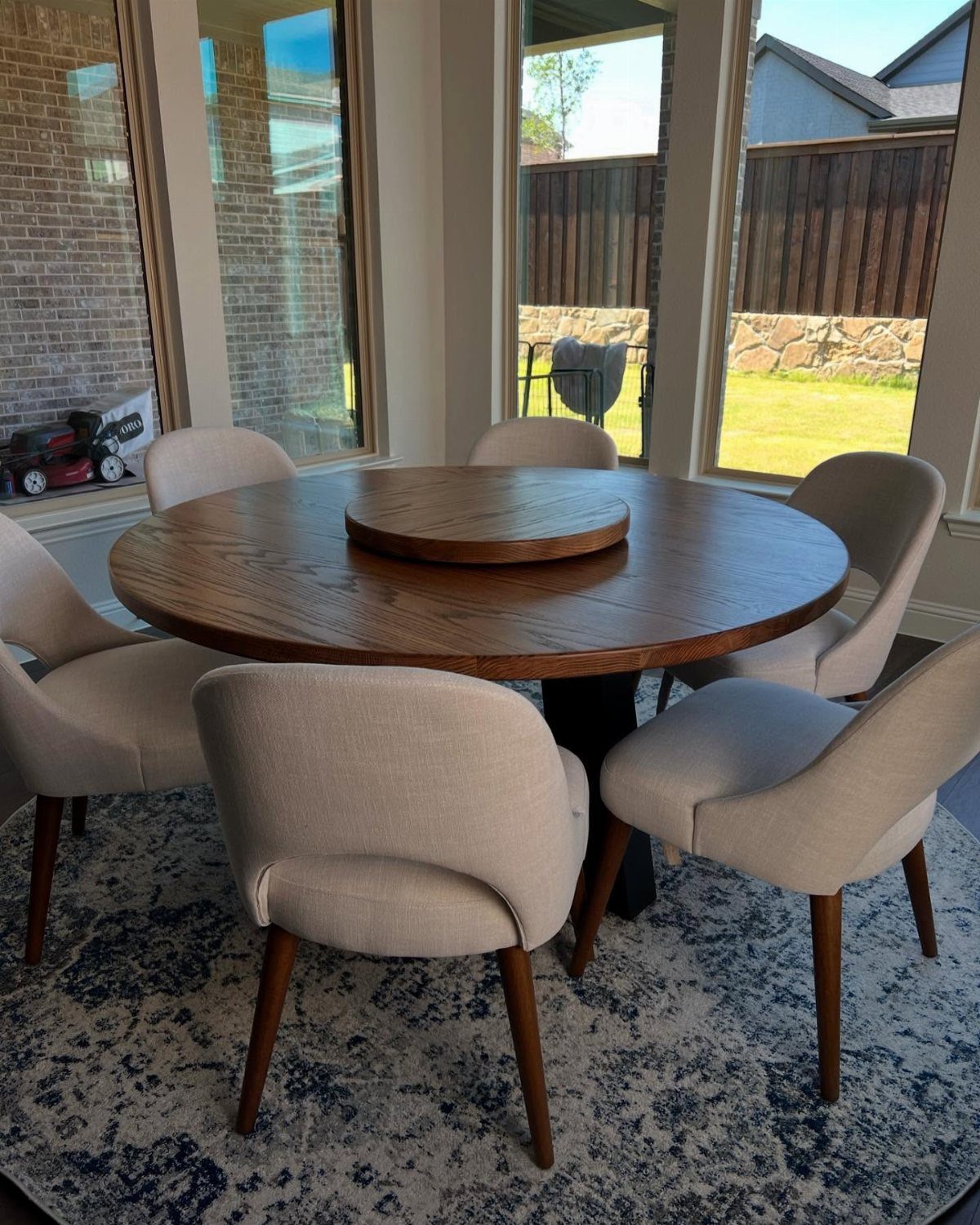 Round wooden dining table with beige chairs on a blue patterned rug.