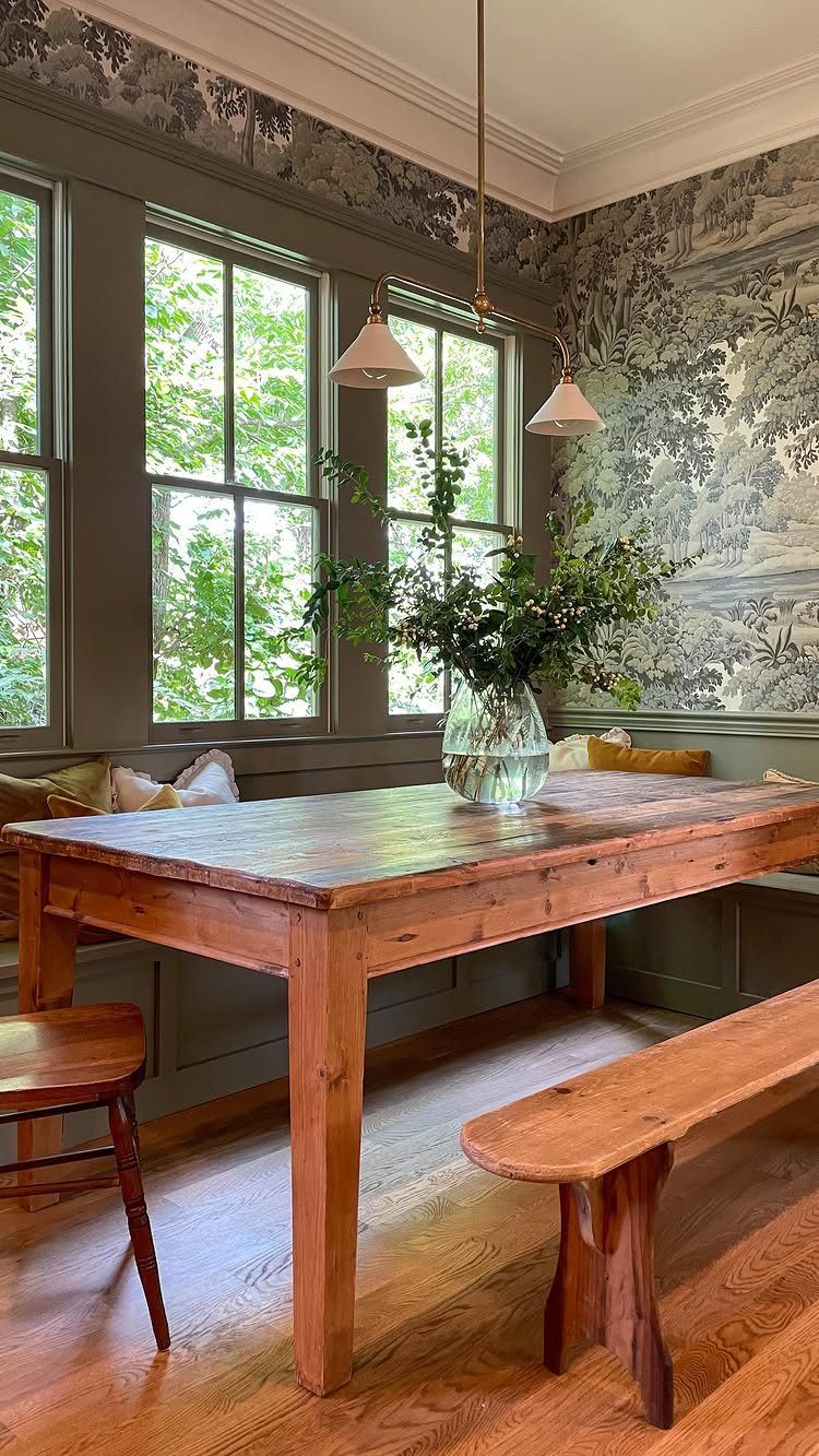 Wooden dining table and bench in a cozy nook with patterned wallpaper.