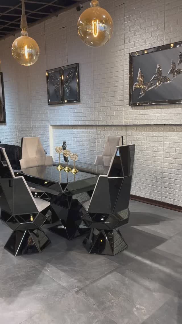 Modern dining room with glossy black geometric table, angular chairs, and gold pendant lights.