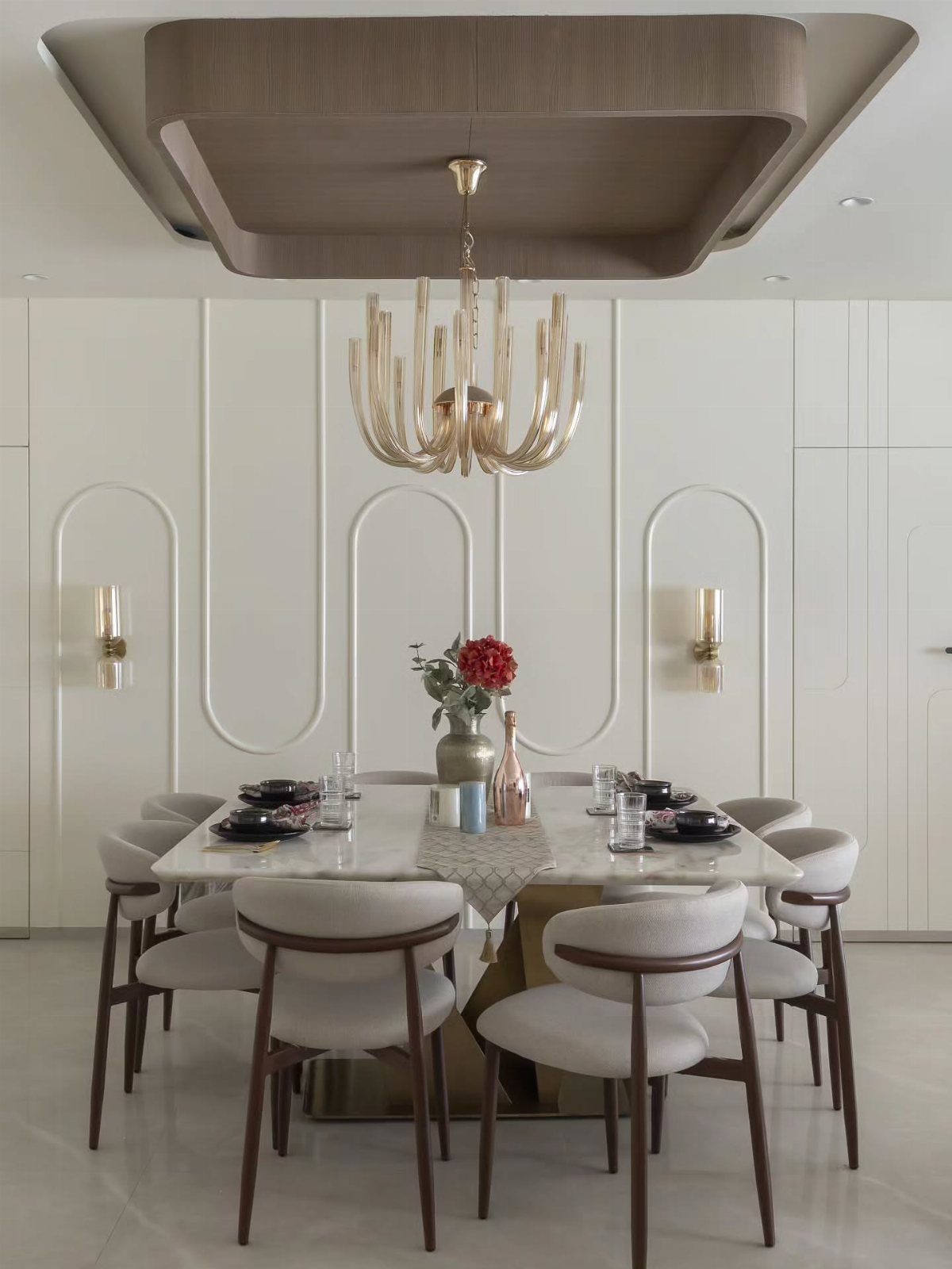 Rectangular marble dining table with sculpted grey chairs under a gold chandelier.