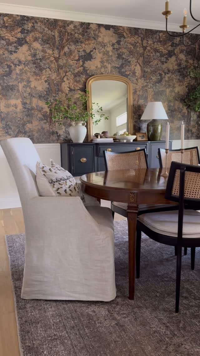 Dining room with forest-patterned wallpaper, round wooden table, and blue sideboard.