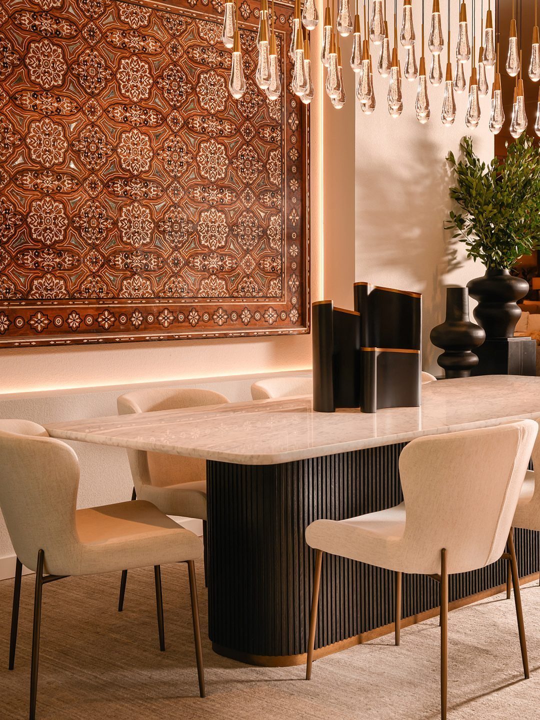 Marble dining table with cream upholstered chairs and a large patterned wall tapestry.