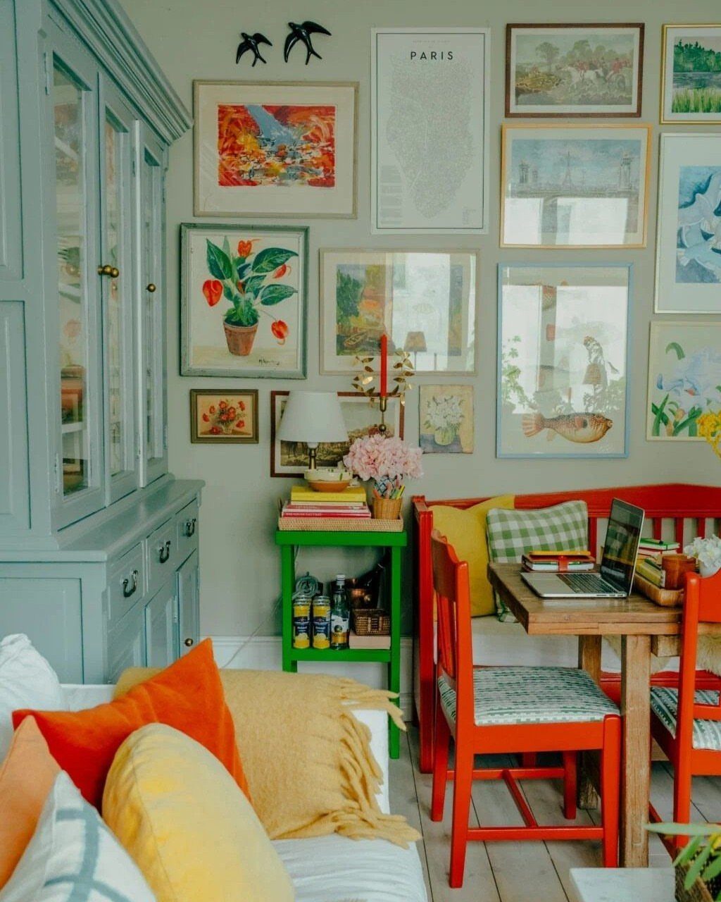 Dining area with a colorful gallery wall and red chairs by a wooden table.