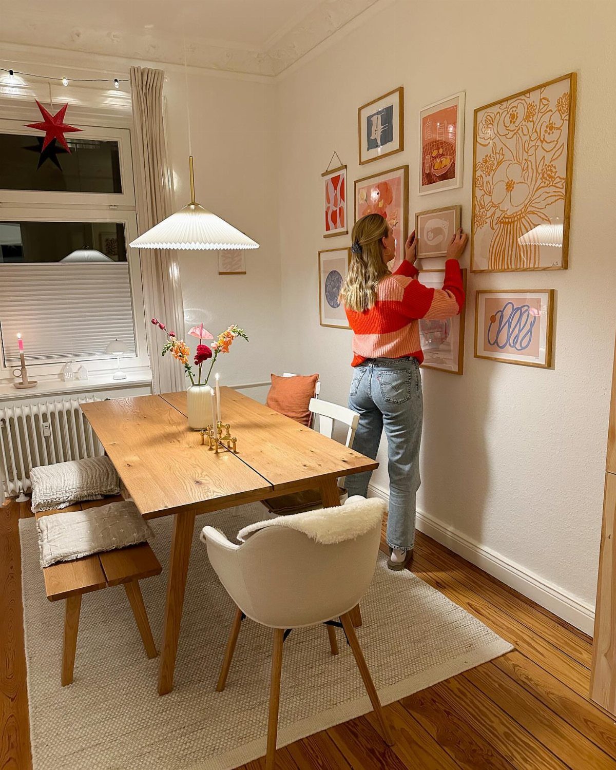 Woman hanging an eclectic collection of framed art on a white dining room wall