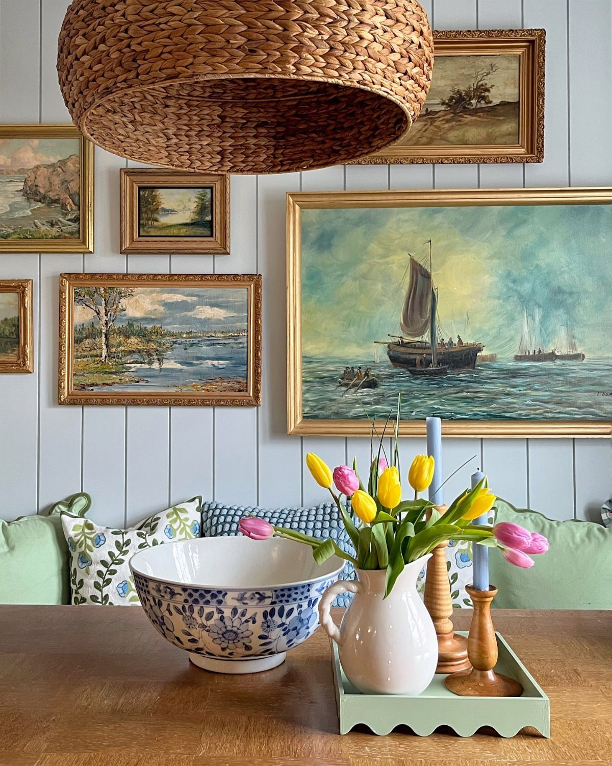 Gold-framed landscape paintings on a blue paneled wall above a dining table with tulips.