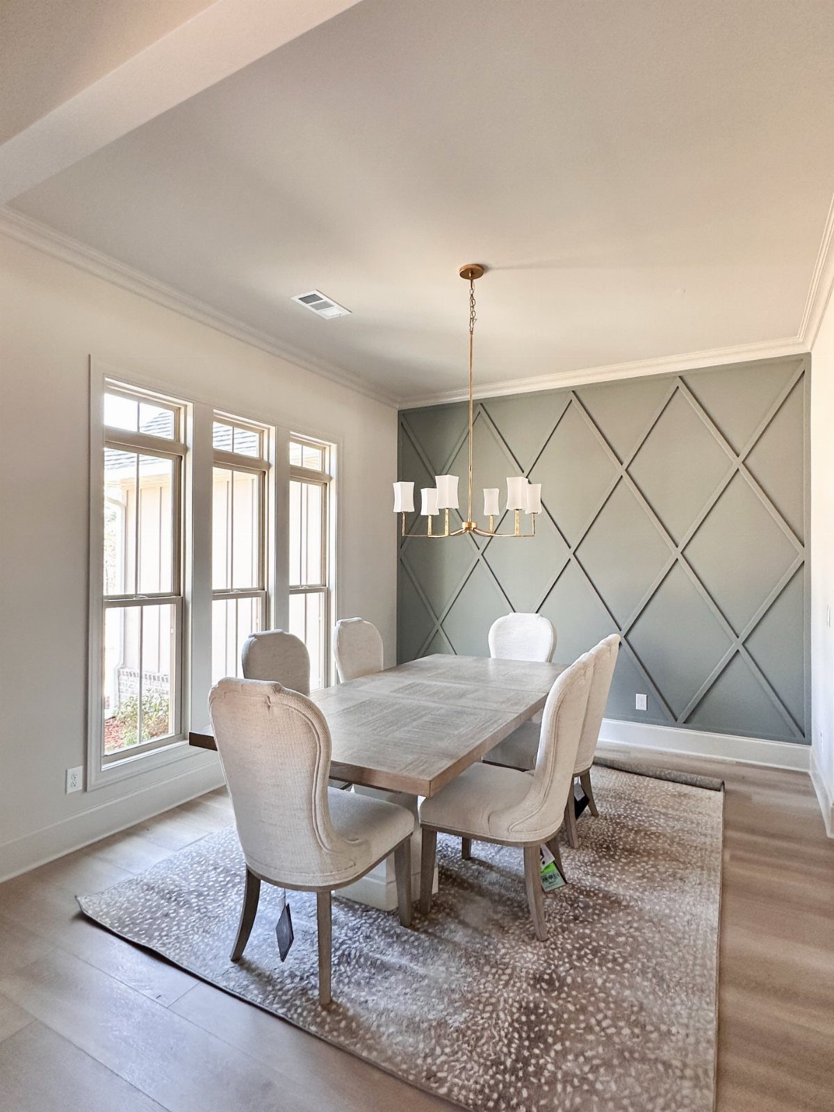 Dining room with a grey-green diamond-patterned accent wall and beige upholstered chairs.