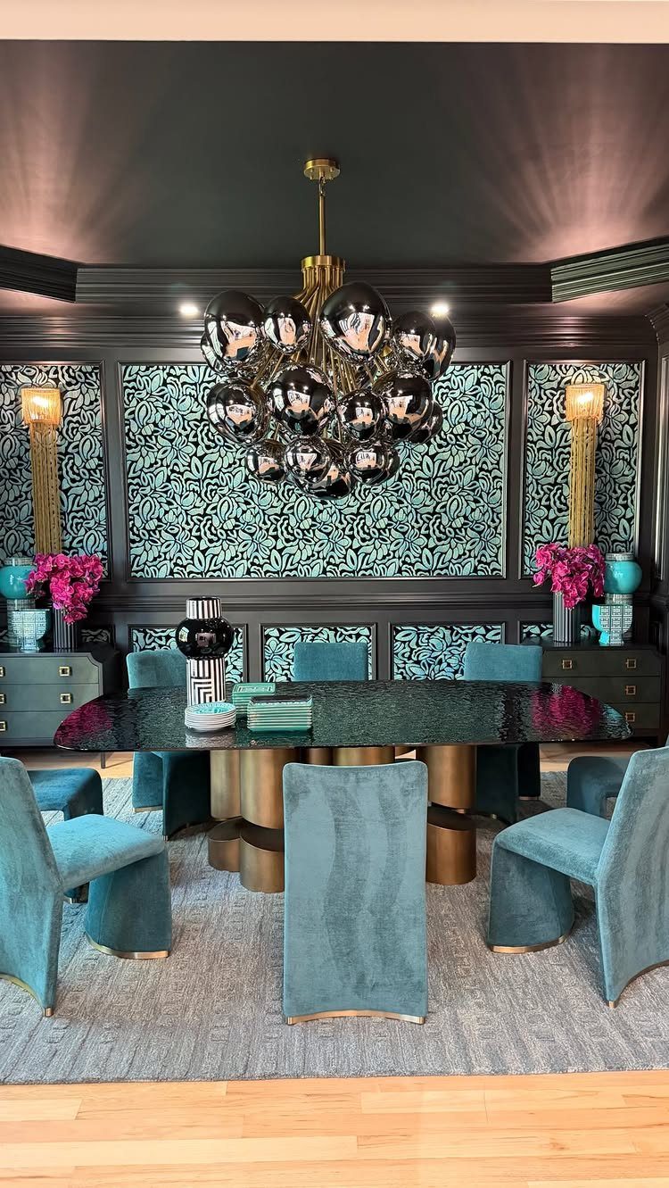 Dining room with teal botanical wallpaper, velvet chairs, and a metallic bubble chandelier.