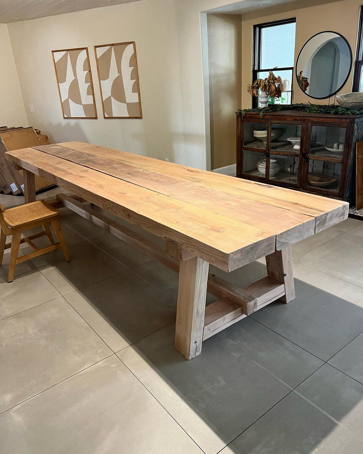 Natural wood trestle table in a dining room with grey tiled floors.
