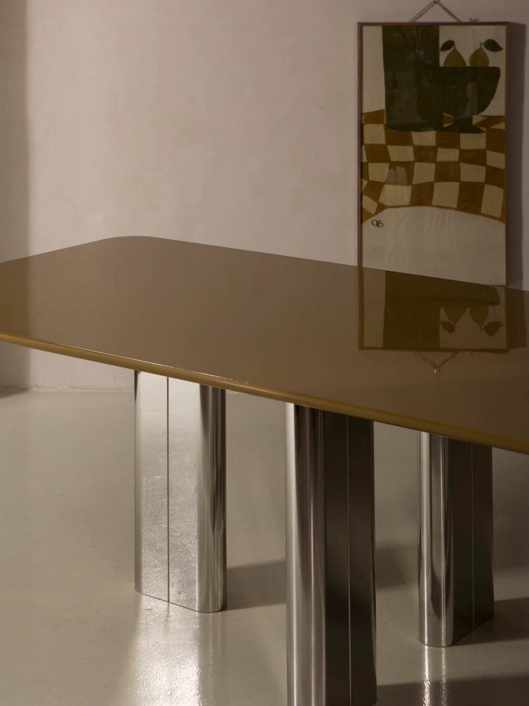 Glossy beige lacquered dining table with polished silver metallic legs in a minimalist room