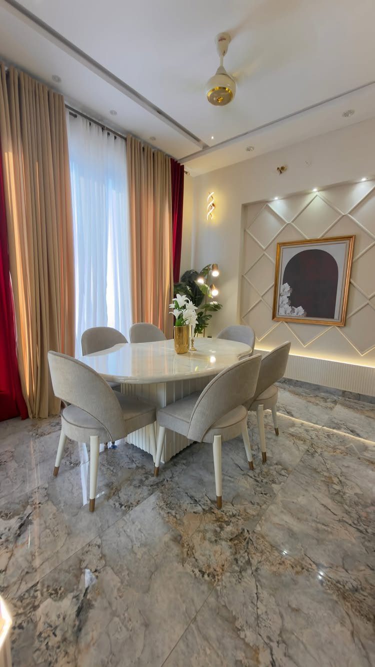 Oval white dining table with upholstered chairs in a modern marble-floored room.