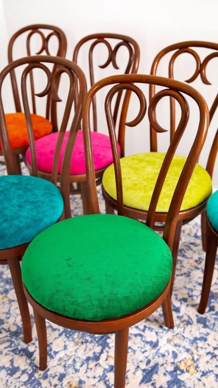 Wooden dining chairs with vibrant multicolored upholstered seats on a patterned rug.