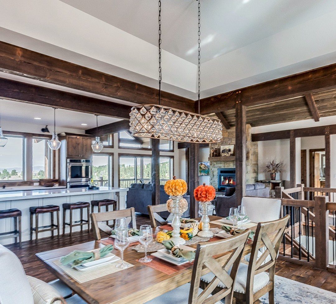 Wooden dining table and living room area separated by dark ceiling beams