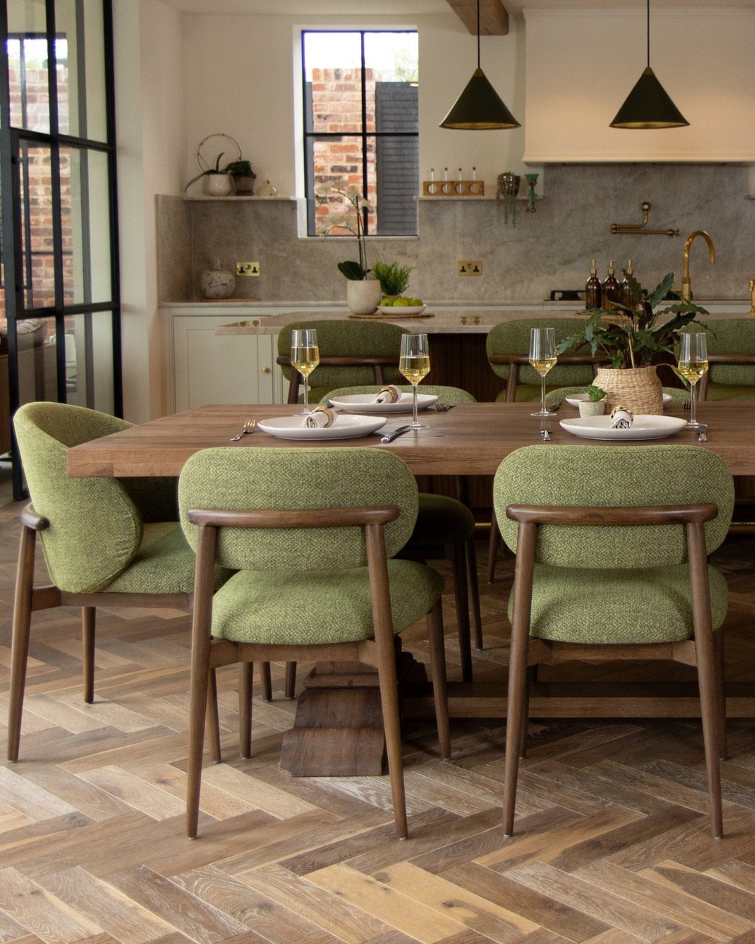 Green mid-century modern dining chairs surrounding a wooden table on herringbone floors.