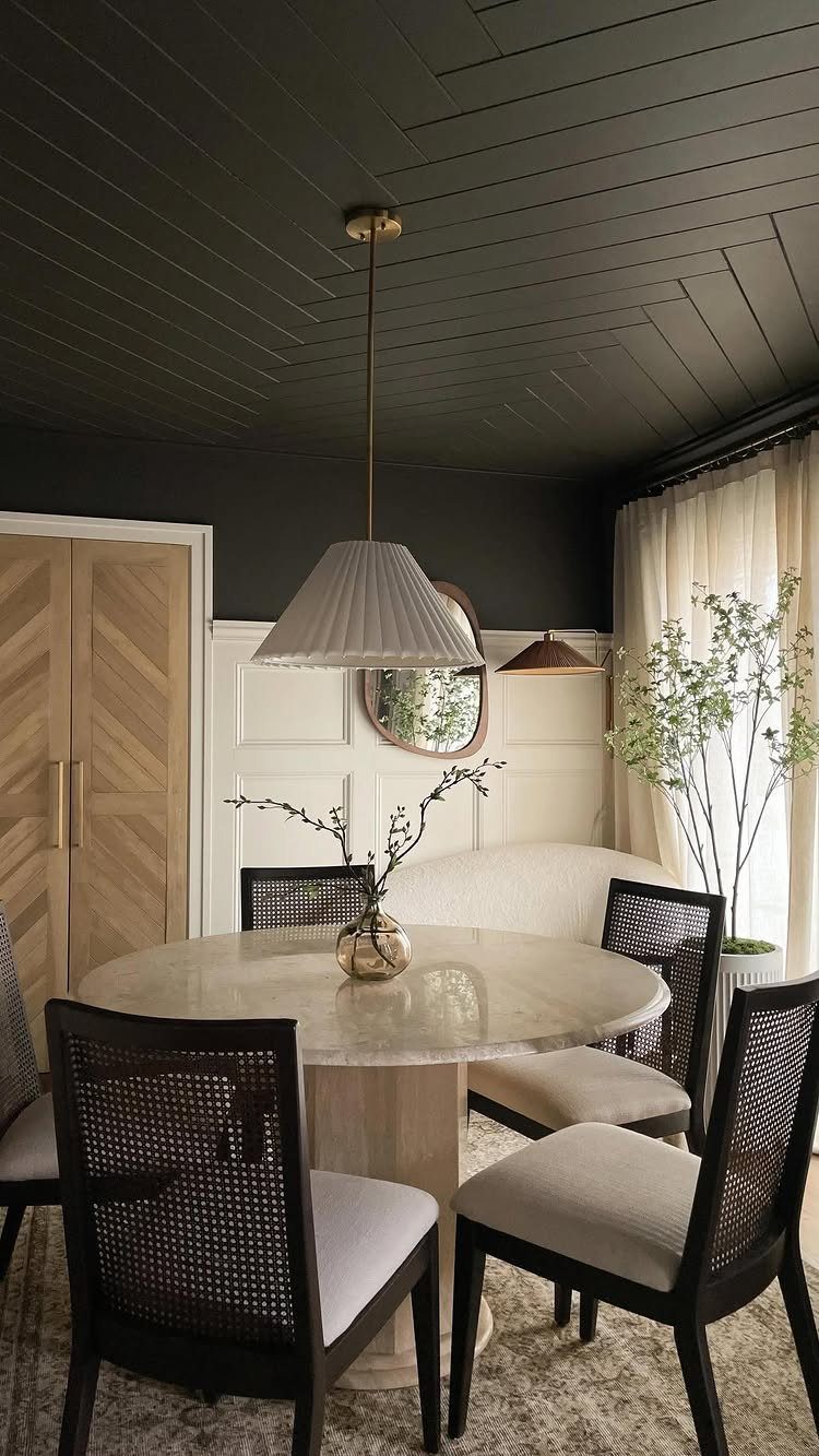 Round marble dining table with cane-back chairs under a black paneled ceiling.