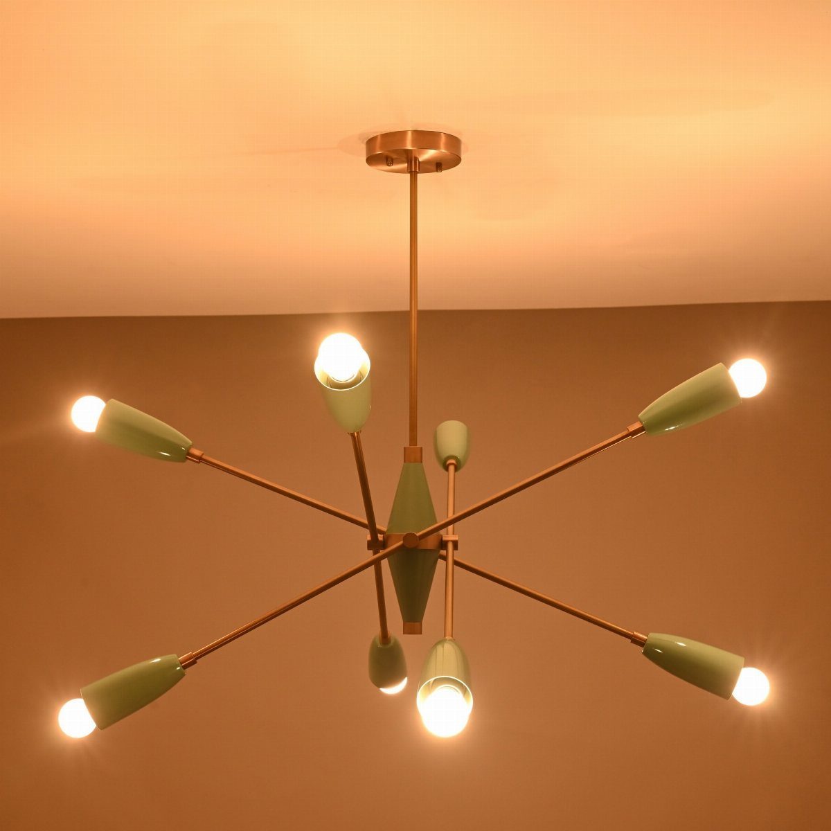 Sputnik chandelier with gold arms and light green shades glowing against a wall.