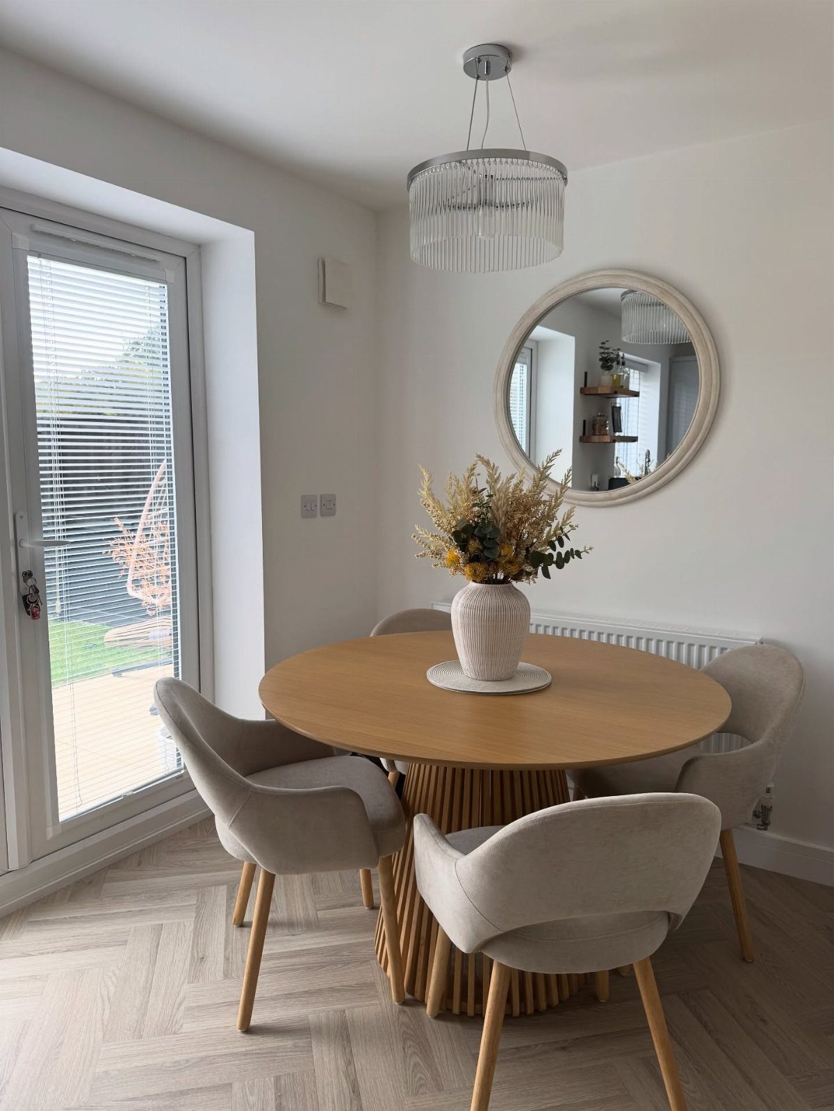 Round wooden dining table with cream chairs and a circular wall mirror.