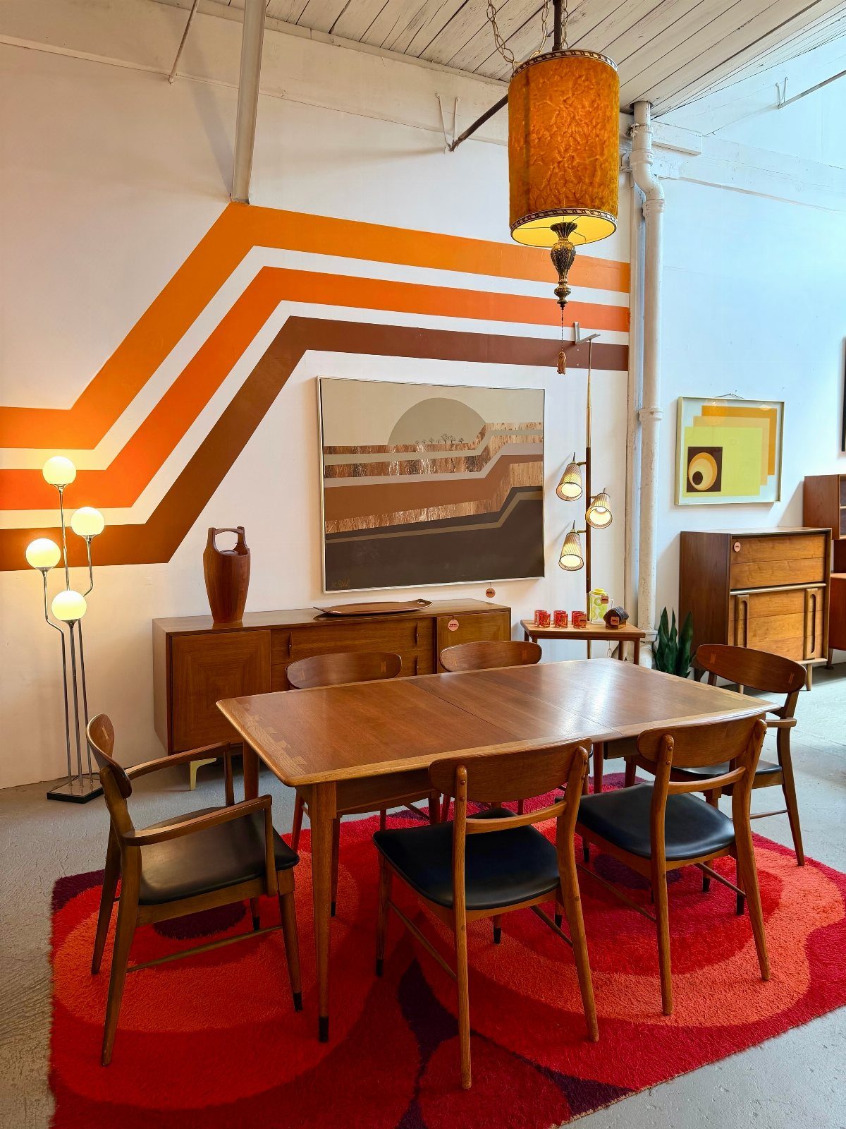 Mid-century dining room with walnut furniture, red rug, and orange striped wall decor.