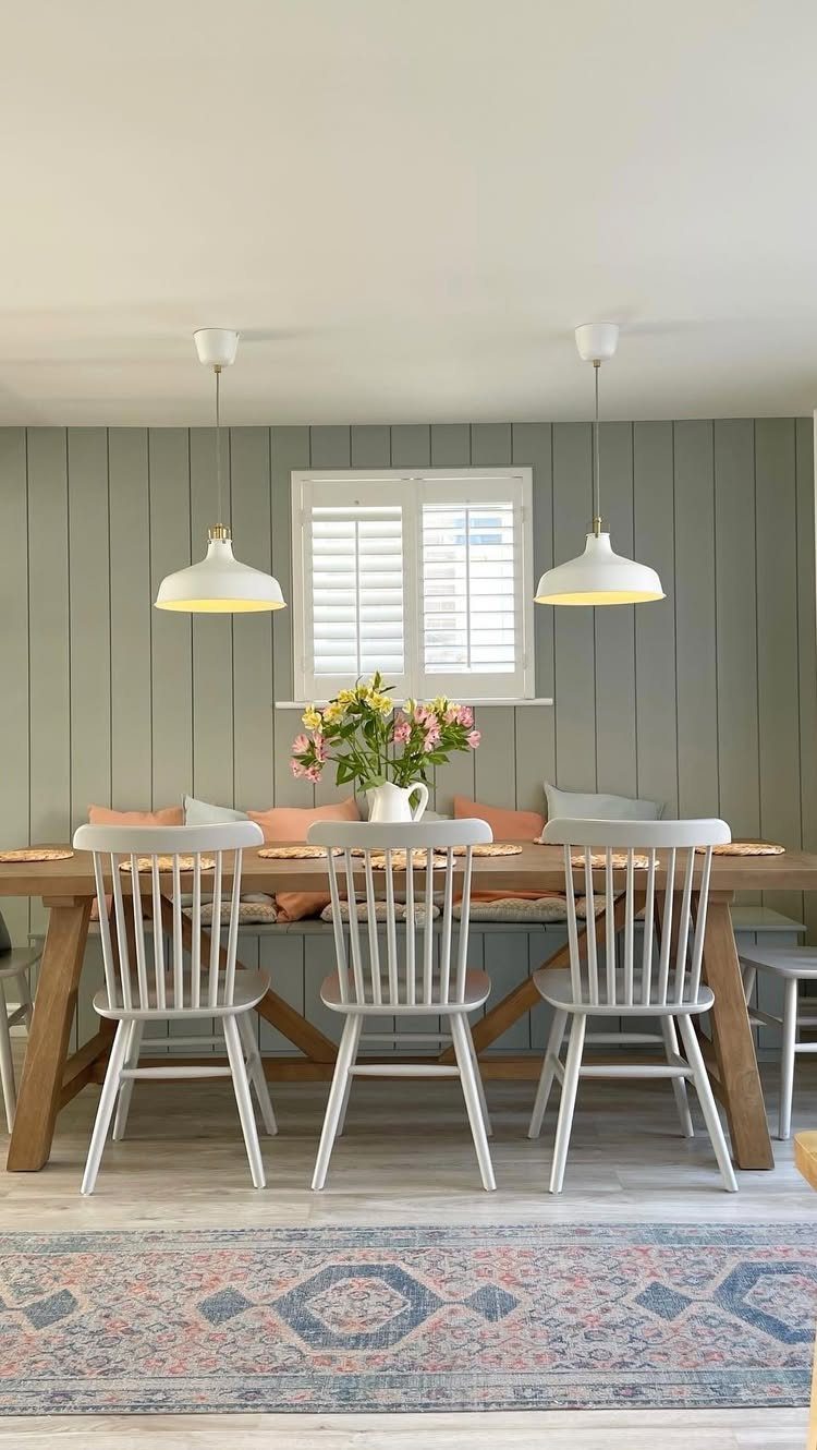 Wooden dining table with white chairs and a built-in banquette seat against green walls.