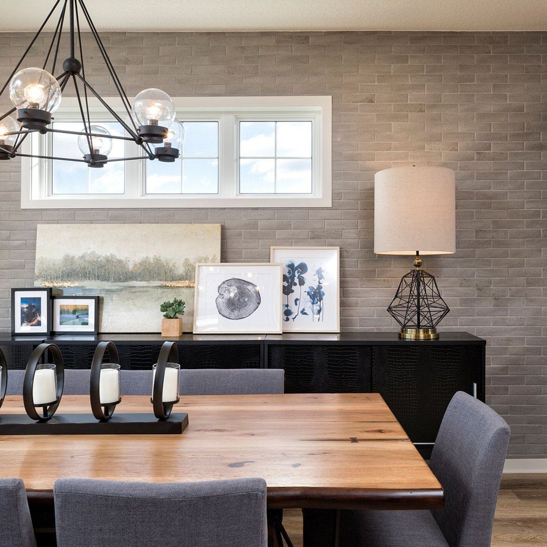Wooden dining table with grey fabric chairs against a grey tiled wall.