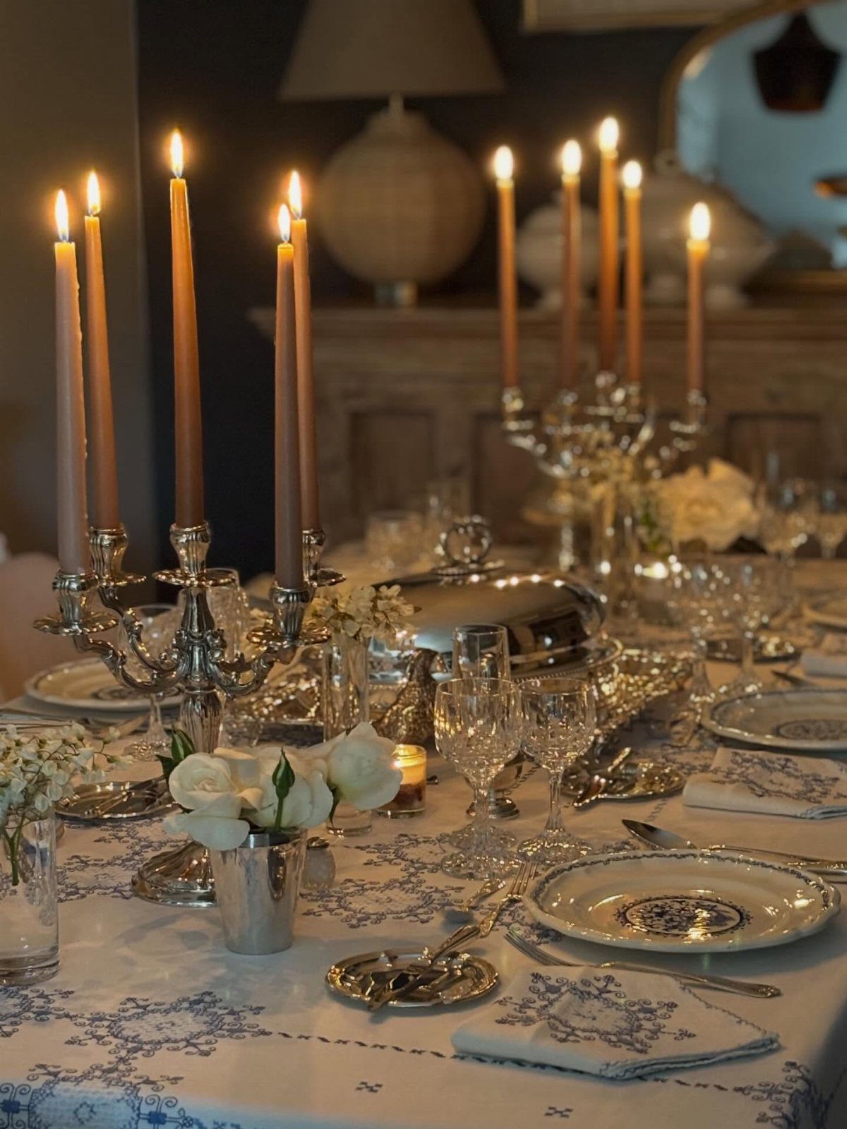 Silver candelabras with lit beige candles and white flowers on a formal dining table
