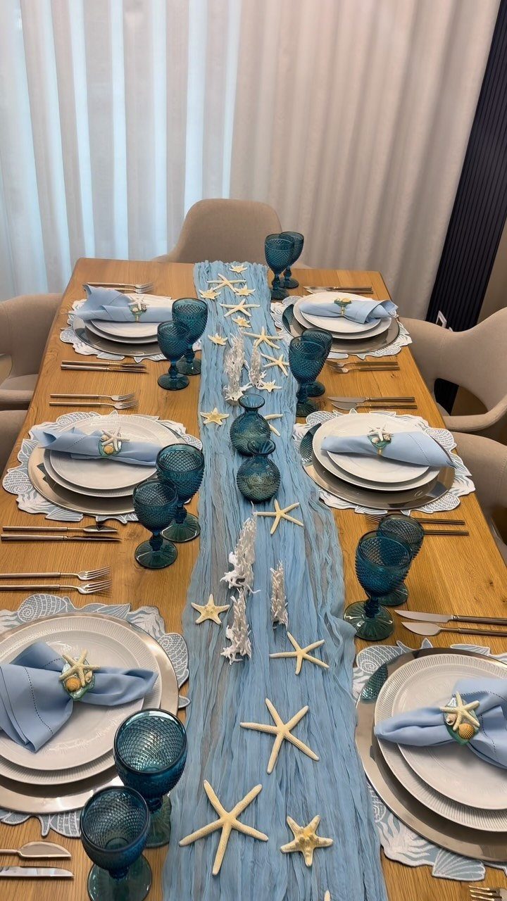 Beach themed dining table centerpiece with blue runner, starfish, and blue glassware.