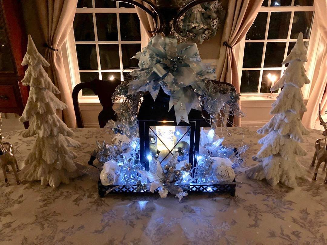 Black decorative lantern with a lit candle and blue bow on a dining table.
