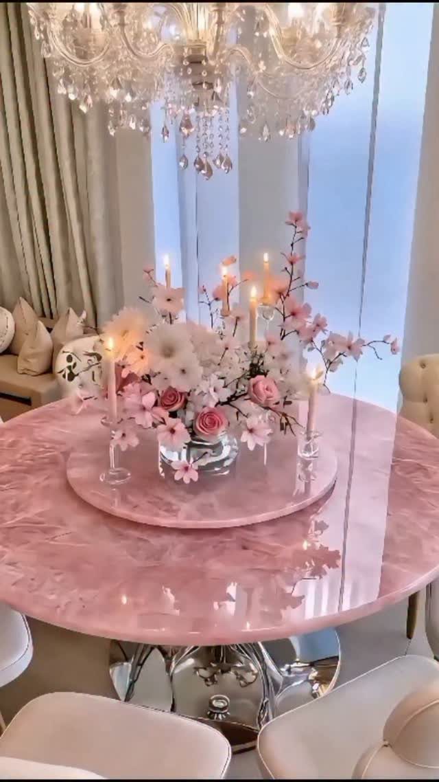 Pink marble table centerpiece with white flowers and lit taper candles on a tray.