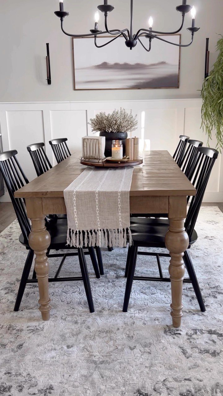 Wooden dining table with a centerpiece tray containing a vase, books, and candle.