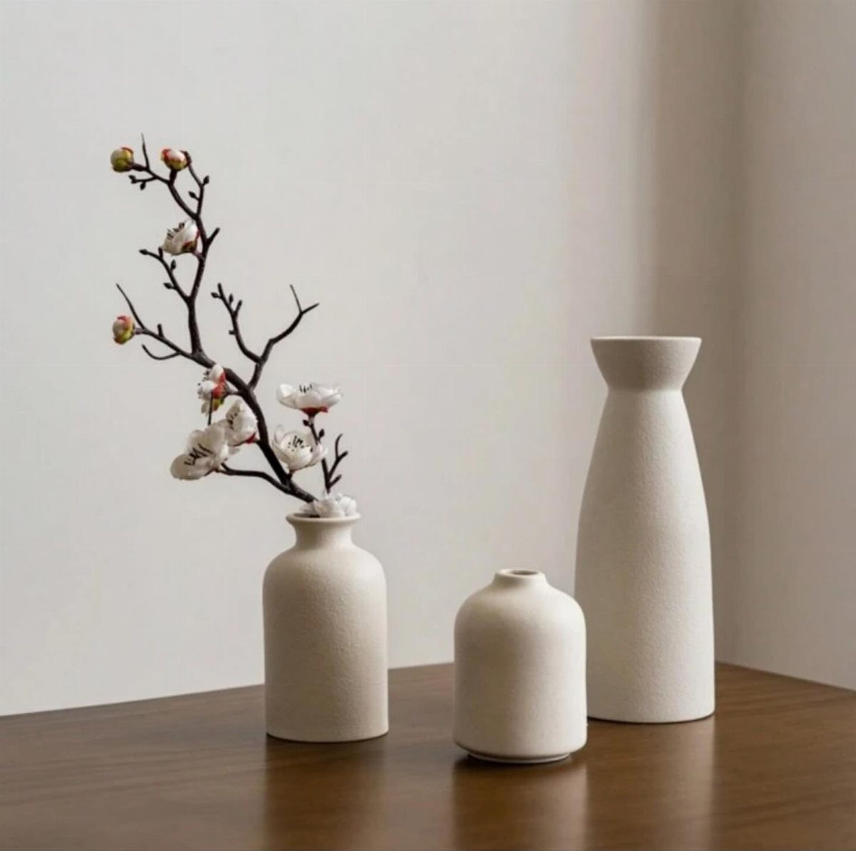 Three white ceramic vases with a flowering branch on a wooden table.