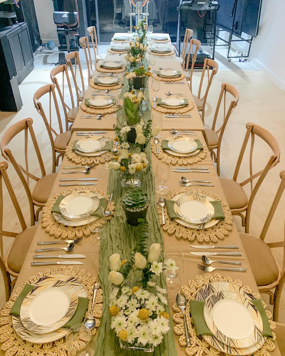 Dining table set with tan tablecloth, green runner, and floral centerpieces.