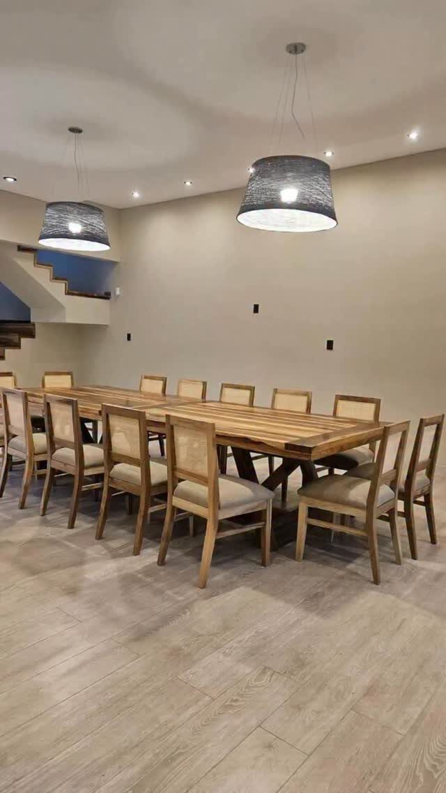 Long wooden dining table with twelve matching chairs under two grey pendant lights.