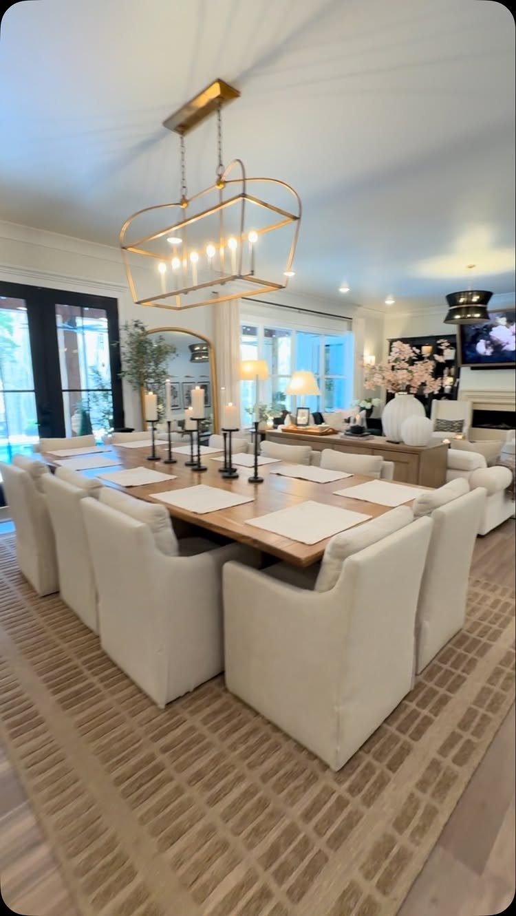 Long wooden dining table with twelve white chairs under a gold chandelier.