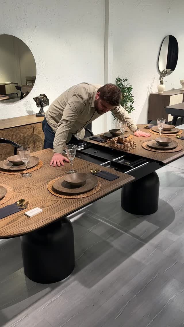 Man adjusting a brown wooden extendable dining table set with plates and glassware.