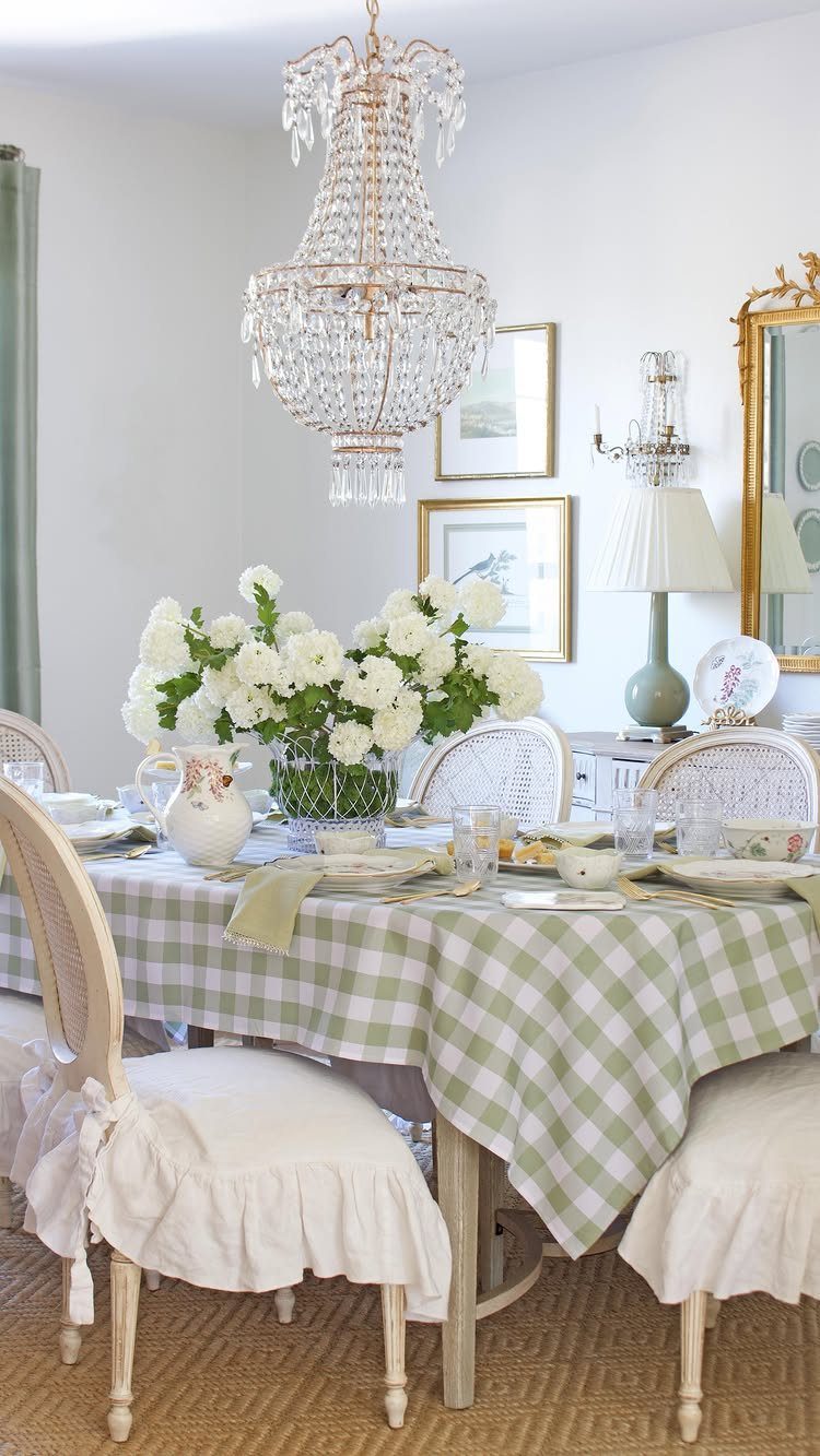 Dining table with green checkered cloth, white flowers, and a crystal chandelier above.