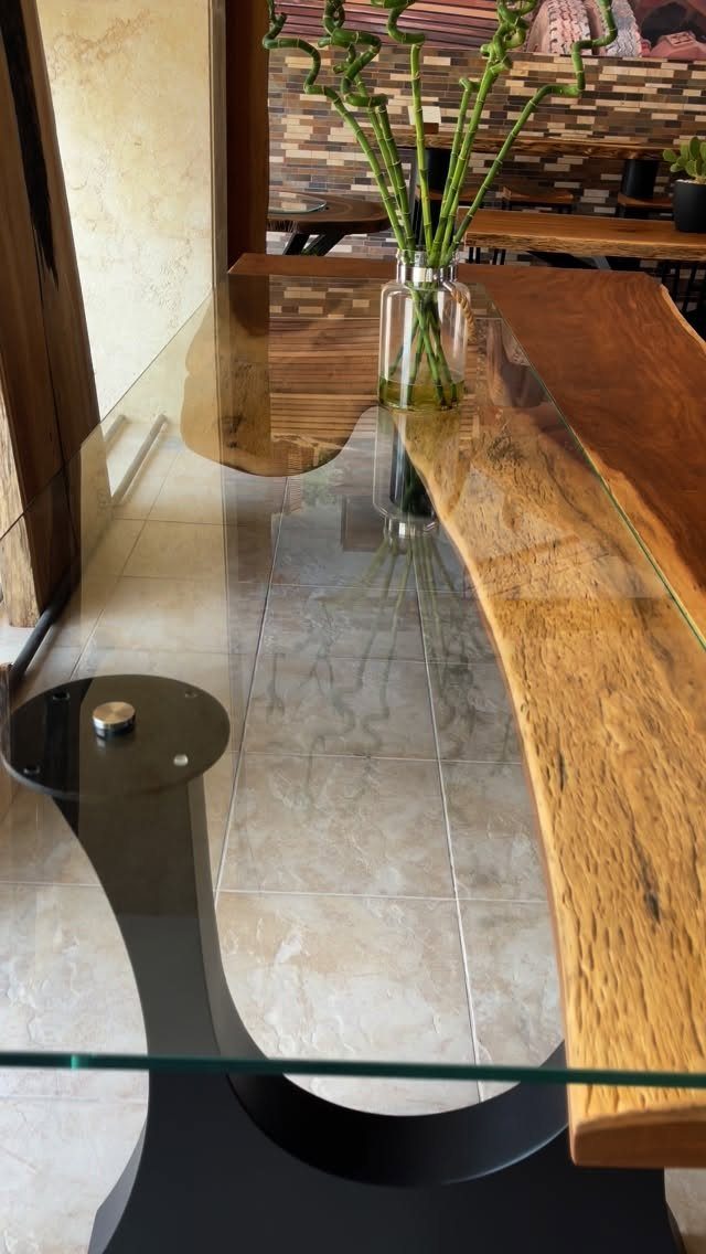 Live-edge wooden slab and glass dining table with a black curved base.