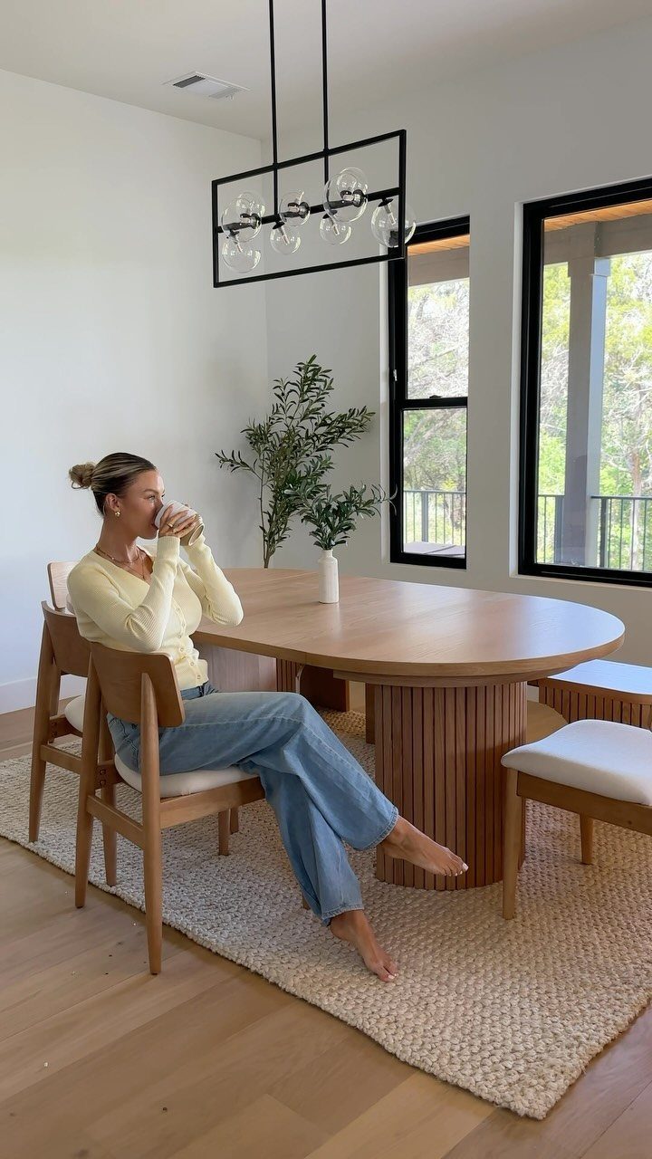 Woman sitting at an oval wooden dining table in a modern, bright room.