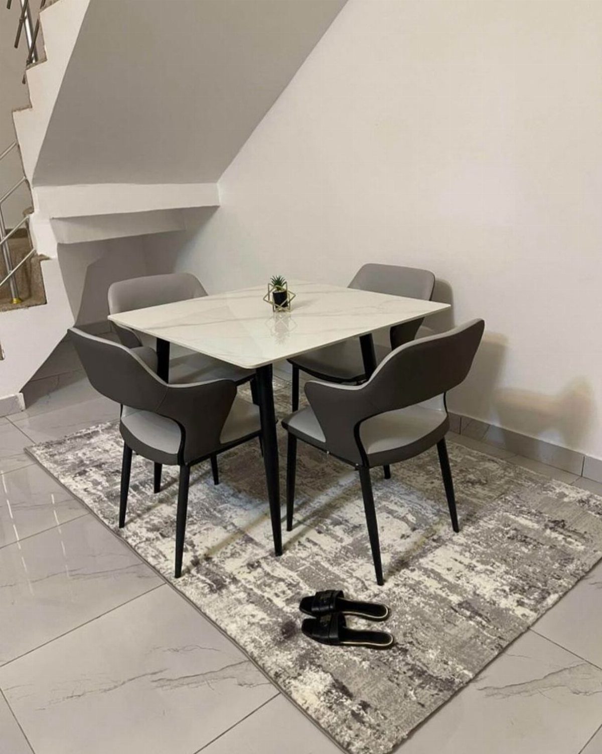 Square white marble dining table with grey chairs on a patterned grey rug.