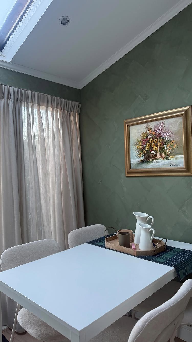 Olive green dining room walls with a white table and floral wall art.