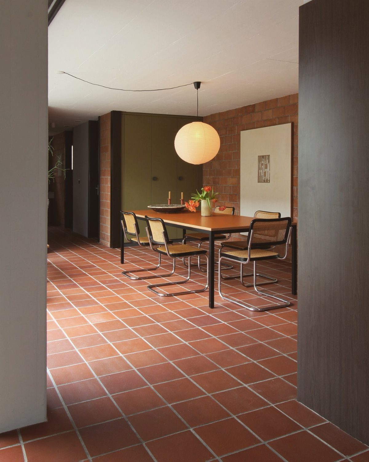 Terracotta brick wall and tiled floor in a dining room with wooden table.