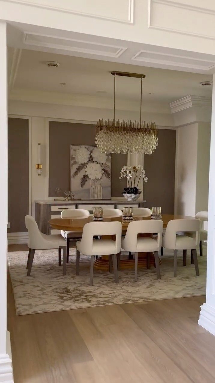 Dining room with a brown accent wall, floral artwork, and crystal chandelier.