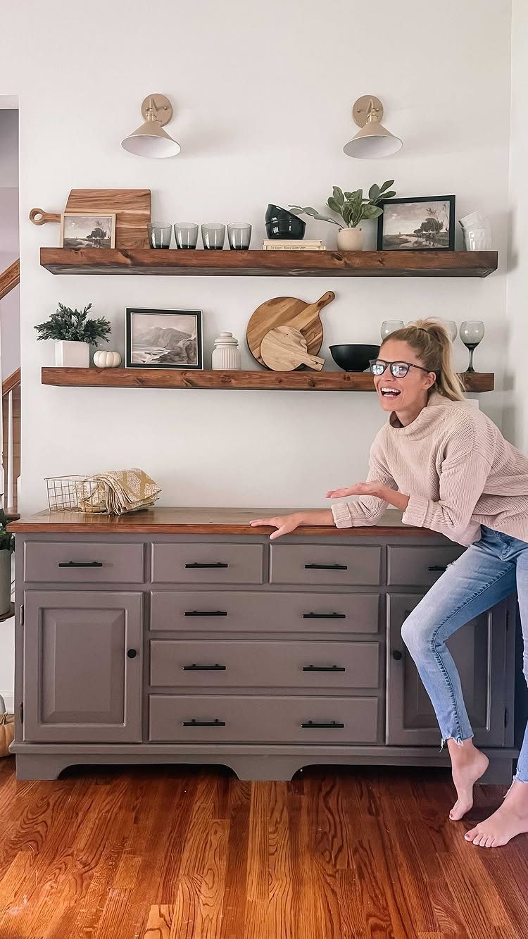 Two dark wood floating shelves with decor above a grey sideboard and white walls