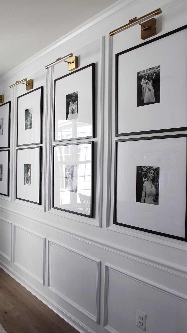 Black and white framed photos in a grid on a white paneled wall.