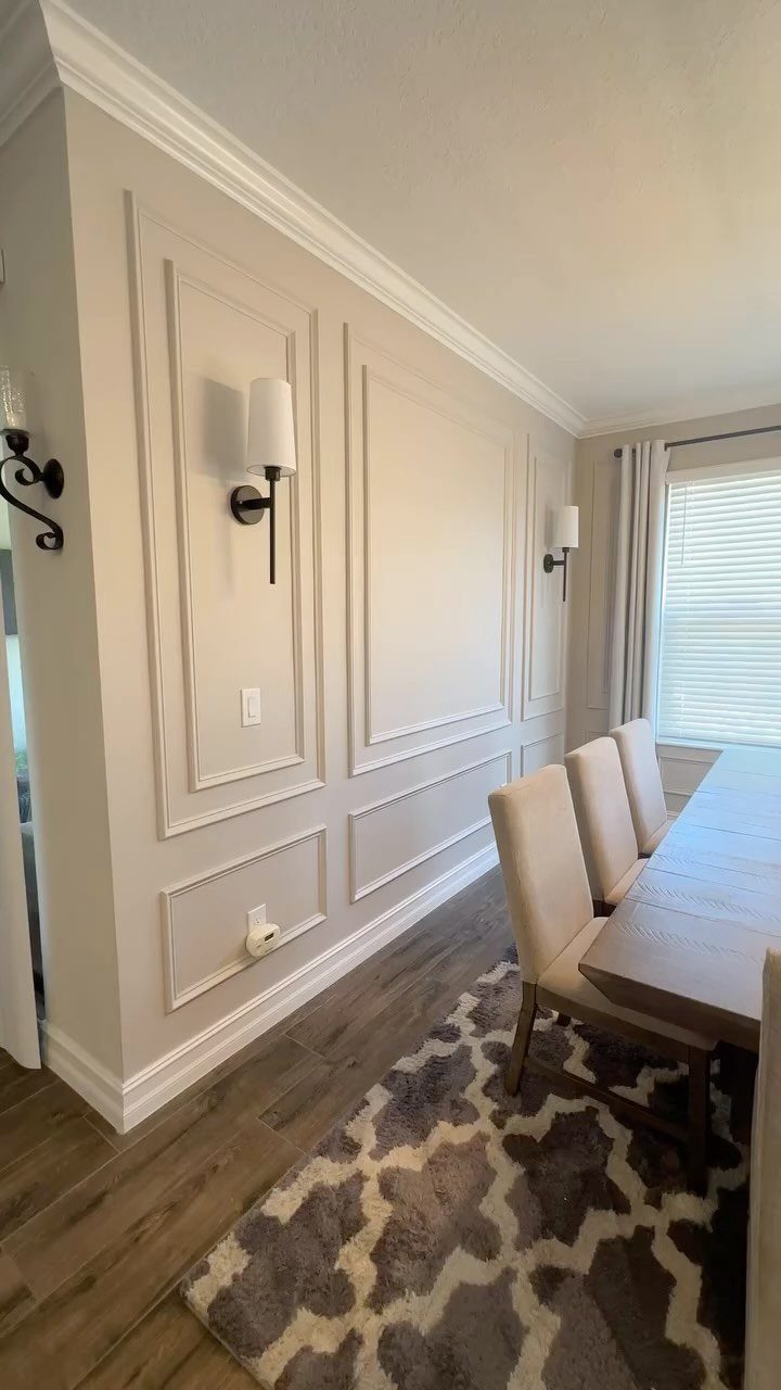 Beige dining room wall with decorative picture frame molding and wall sconces.