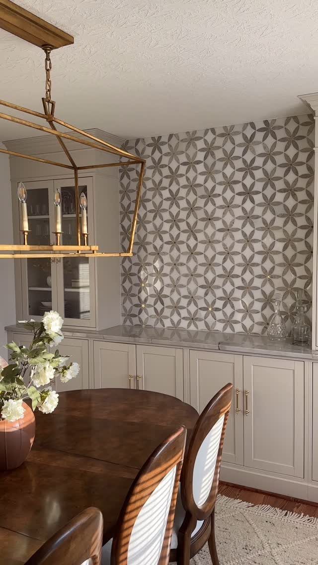 Light-grey built-in buffet in a dining room with patterned wallpaper and wooden table.