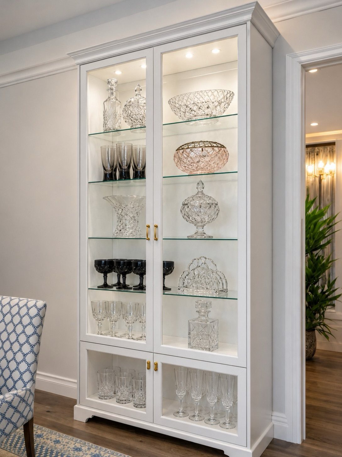 White glass-fronted display cabinet filled with crystal glassware and bowls in a dining room.