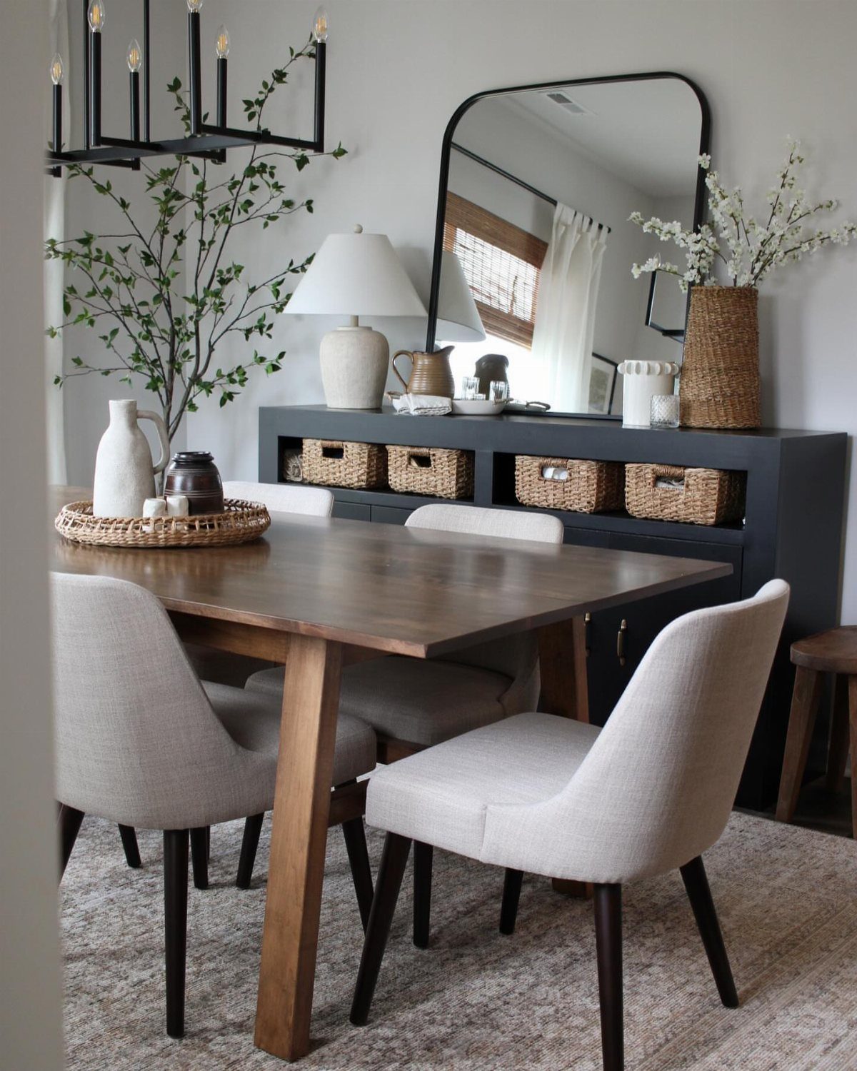Wooden dining table and chairs next to a dark grey buffet with arched mirror.