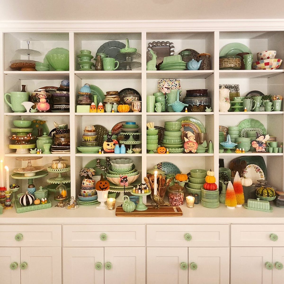 White built-in buffet shelves filled with green and brown ceramic tableware and pumpkins.
